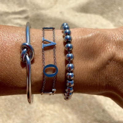 Três pulseiras prateadas num pulso com fundo de areia