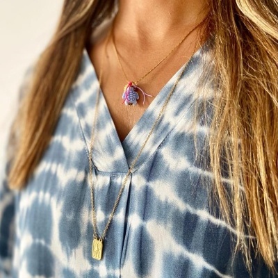 Colar duplo dourado com pedras e placa retangular em pessoa com blusa azul tie-dye