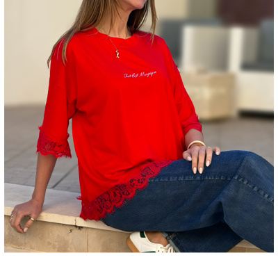 T-shirt feminina vermelha com renda e texto bordado, jeans azul e ténis brancos em ambiente exterior.