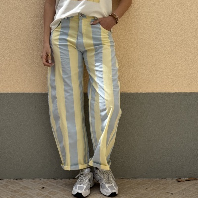 Calças compridas de algodão riscas azuis e amarelas com botão, usadas com t-shirt branca e ténis, parede bicolor
