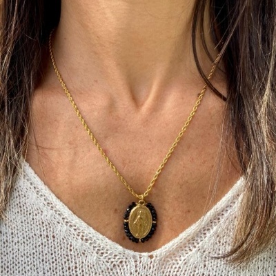 Colar dourado com pendente oval e pedras pretas em pescoço de pessoa com camisola branca