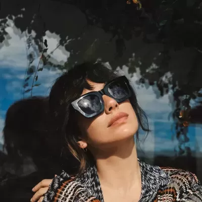 Mulher com óculos de sol pretos e casaco de padrão às riscas em fundo refletivo escuro