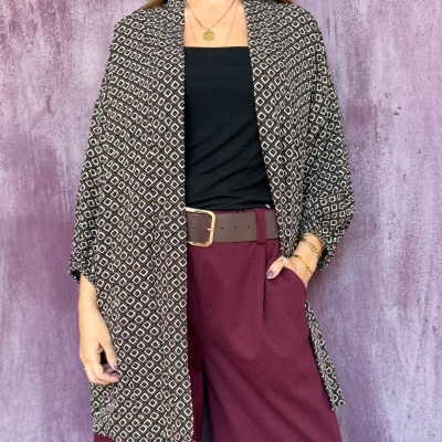 Pessoa veste kimono padrão geométrico castanho e branco, top preto e calças vinho com cinto castanho, fundo roxo.