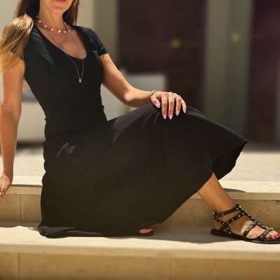 Mulher com vestido preto curto e sandálias pretas com tachas sentada