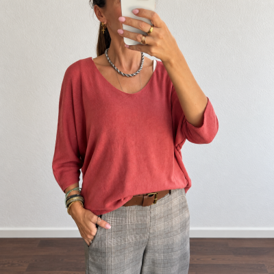 Mulher com camisola vermelha e calças cinza às riscas numa sala interior