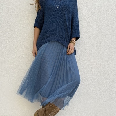 Look com top de malha azul, saia plissada azul e botas castanhas bordadas.