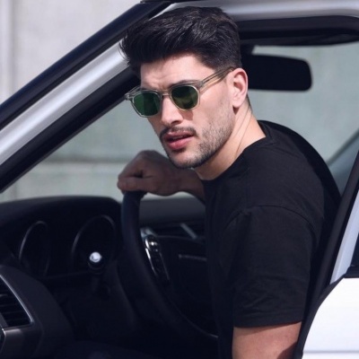 Homem de óculos de sol sentado ao volante de carro branco.