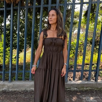 Mulher a usar vestido castanho longo com alças e franzidos em ambiente exterior