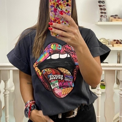 Pessoa com T-shirt preta com estampa de boca colorida, óculos de sol em fundo interior