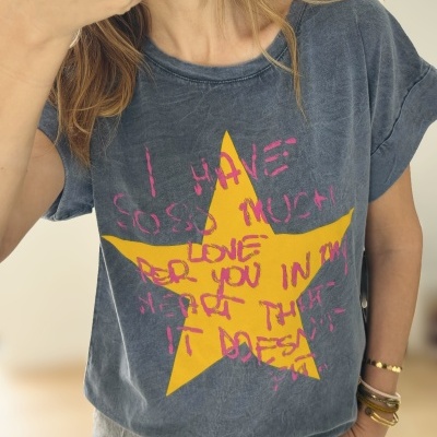 T-shirt azul escura com estrela amarela e texto rosa sendo usada por pessoa com pulseiras e anéis