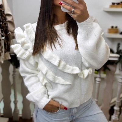 Camisola branca de malha com folhos e calças de ganga claras num ambiente interior.