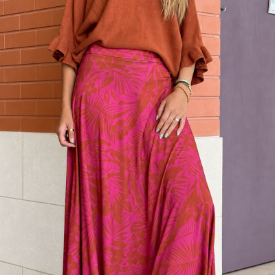 Mulher com camisola castanha, saia comprida vermelha e rosa com padrão floral, e botas castanhas.