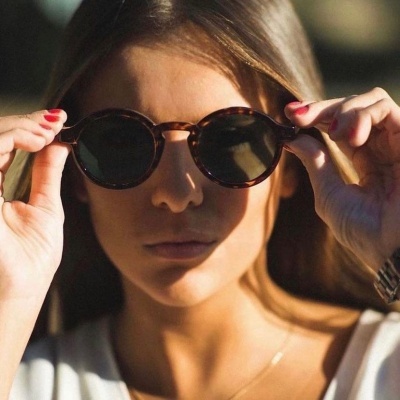 Mulher a colocar óculos de sol redondos castanhos com lentes escuras