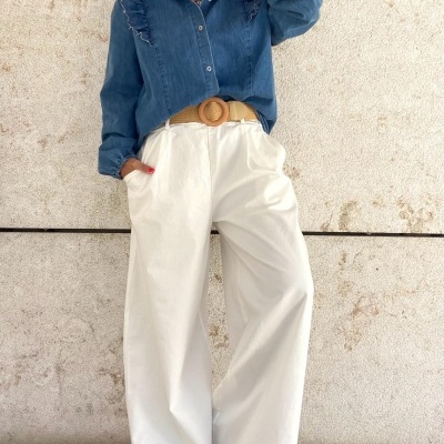 Modelo veste camisa azul de ganga com folhos e calças largas brancas com cinto bege.