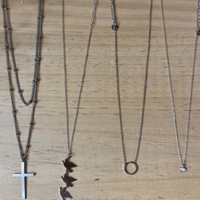 Quatro colares de prata com diferentes pendentes sobre madeira clara.