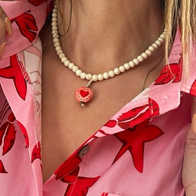 Colar de contas creme com pendente em forma de coração vermelho e rosa no pescoço