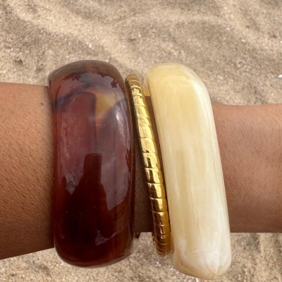 Pulseiras largas castanho, dourado e bege no pulso com fundo de areia