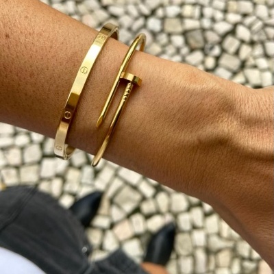 Pulseiras douradas num braço com pavimento de pedras ao fundo