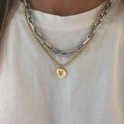 Colares prateado de elos grandes e colar dourado com bolinhas e pendente em forma de coração sobre t-shirt branca
