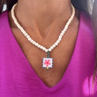 Colar de contas brancas com pendente floral quadrado numa pessoa com blusa roxa