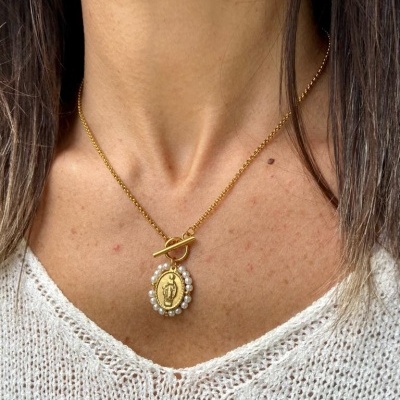 Colar dourado com pendente oval e pérolas em pescoço com camisola branca