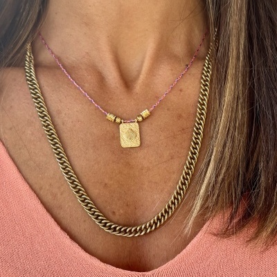 Duas correntes douradas, uma grossa e outra fina com pendente, sobre camisola cor de salmão.