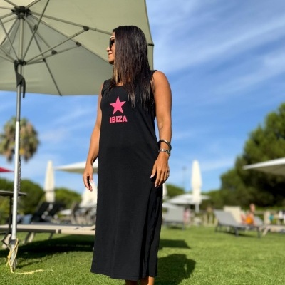 Mulher com vestido longo preto com estrela rosa e texto IBIZA em relvado ao ar livre