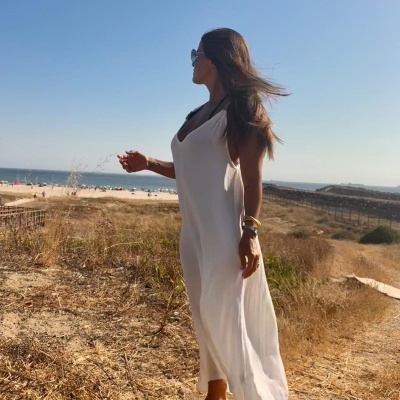 Mulher de vestido branco comprido numa paisagem seca perto do mar com céu azul