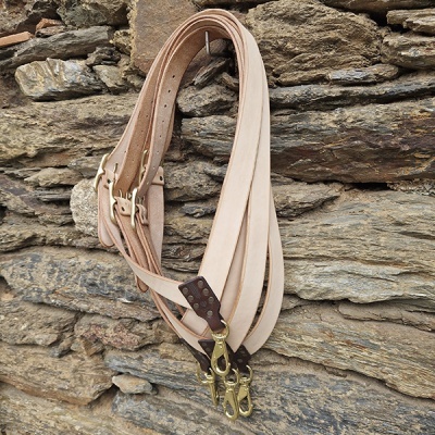 Cintos em pele bege com fivelas douradas pendurados numa parede de pedra