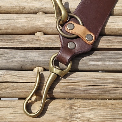 Alça de couro castanho com mosquetão em metal dourado sobre madeira