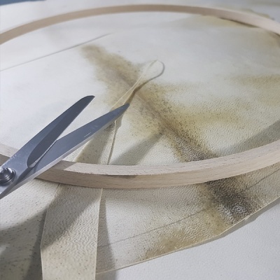 Bastidor de madeira com tecido branco e tesoura metálica.