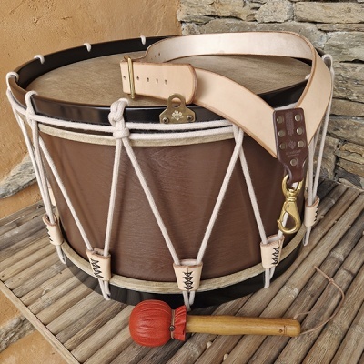 Tambor artesanal em couro castanho com alça bege e baqueta com cabeça vermelha sobre ripas de madeira