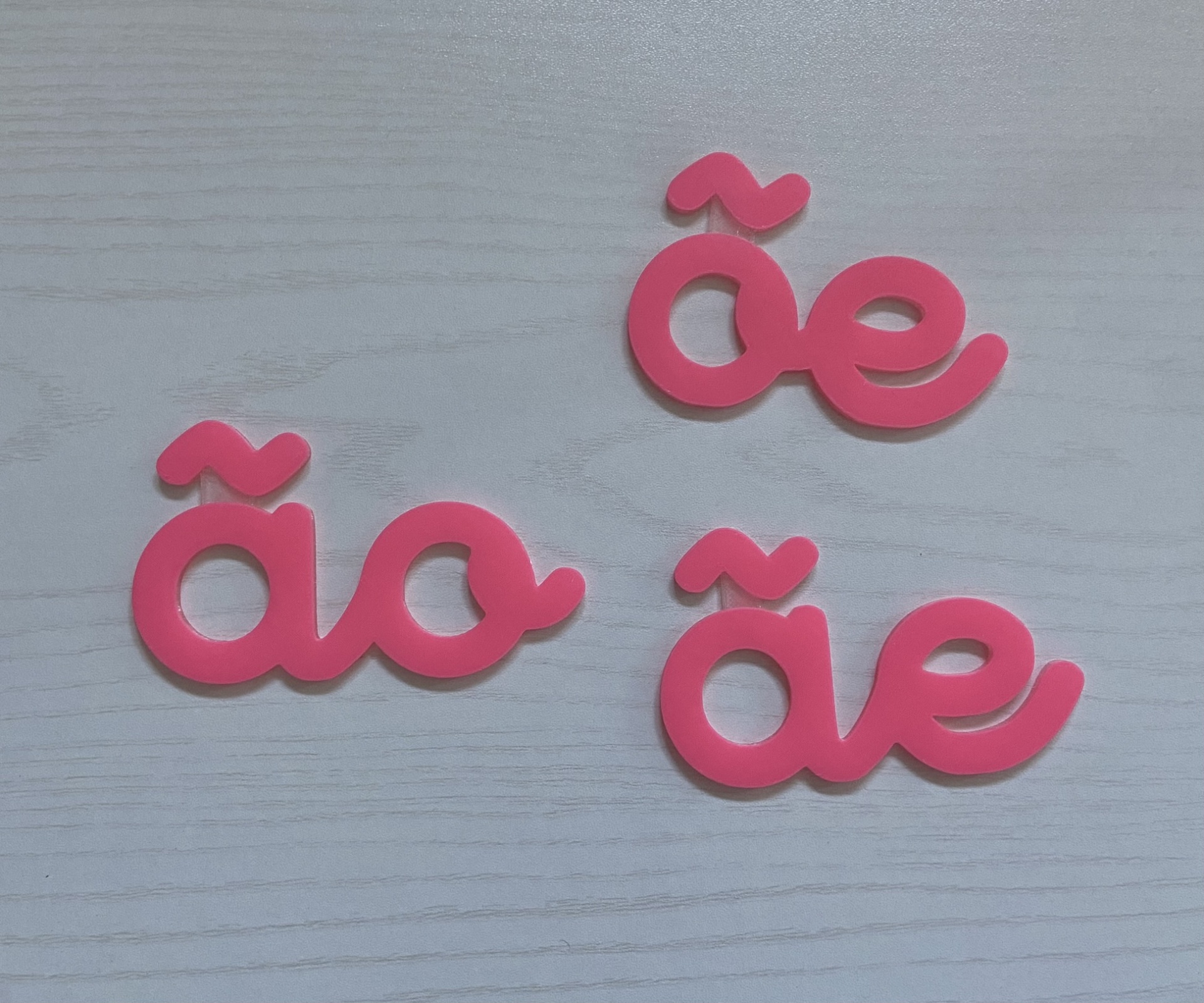 Ditongos # cor de rosa # tamanho grande Três conjuntos de letras cor-de-rosa plástico 'ão', 'õe' e 'ãe' sobre superfície cinza claro