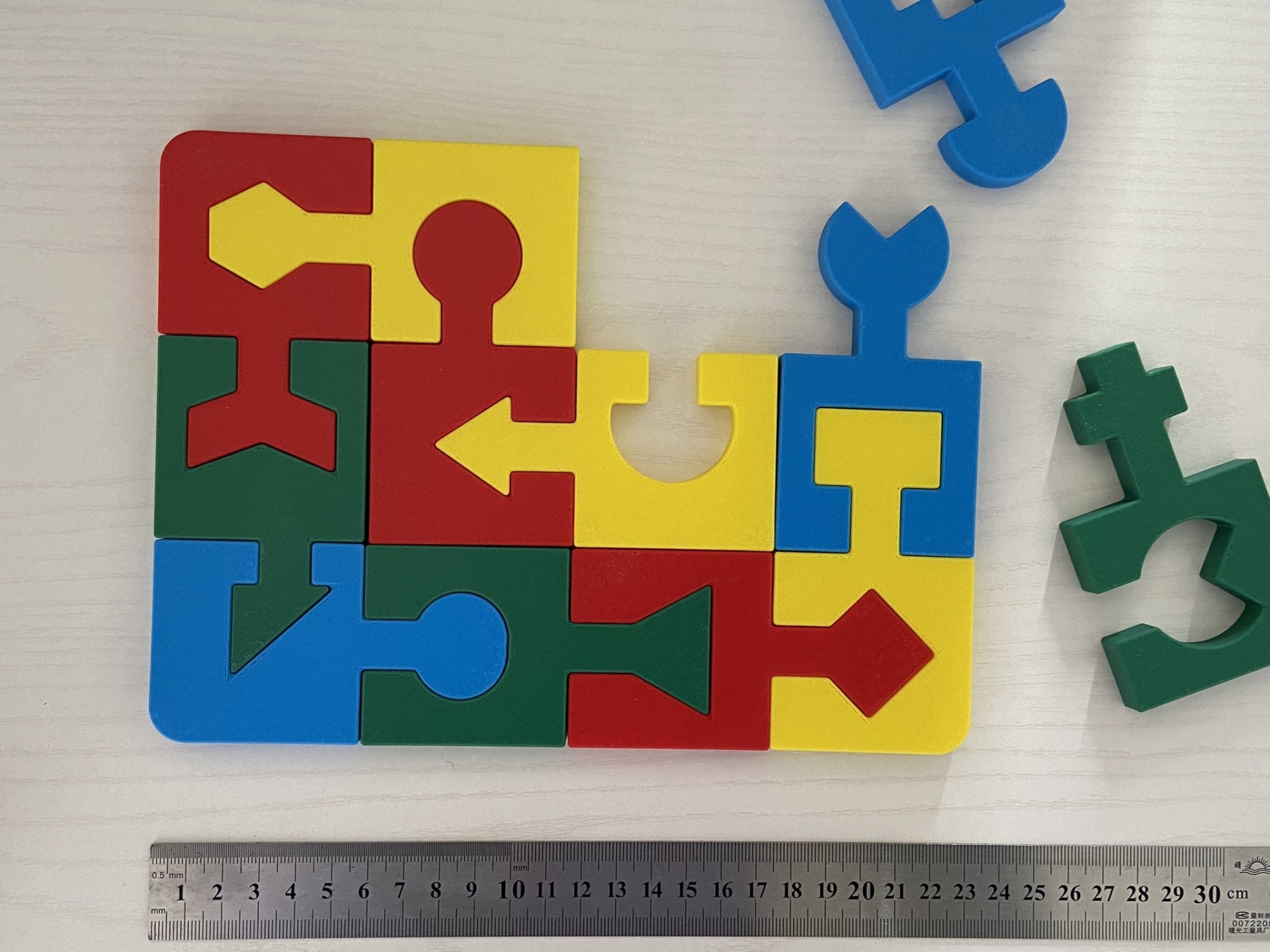 Puzzle educativo # 4 cores Peças de encaixe de madeira coloridas sobre superfície branca com régua metálica ao lado.