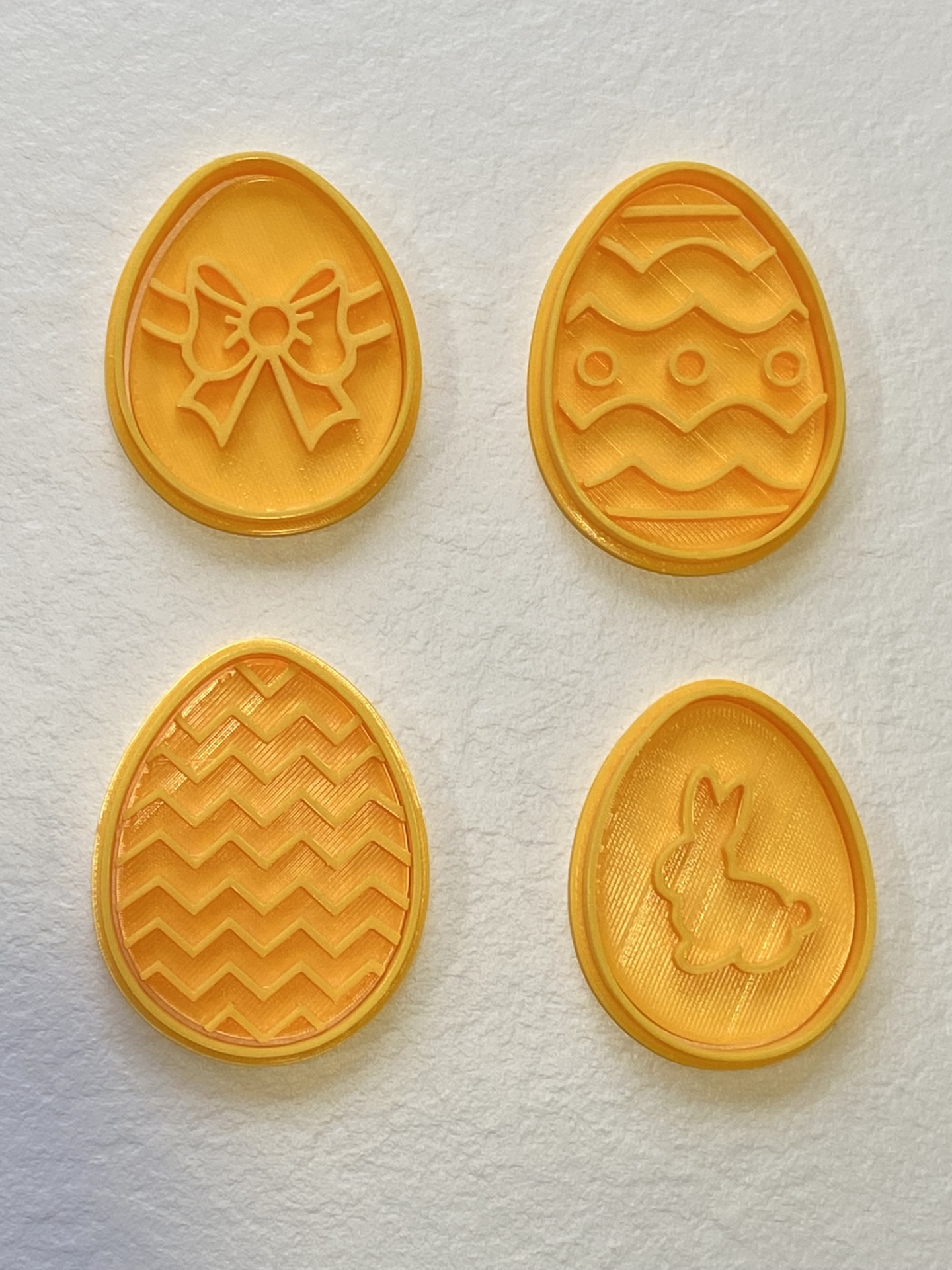 Cortadores # Ovos da Páscoa Quatro moldes amarelos em forma de ovo com padrões de laço, ondas, zig-zag e coelho