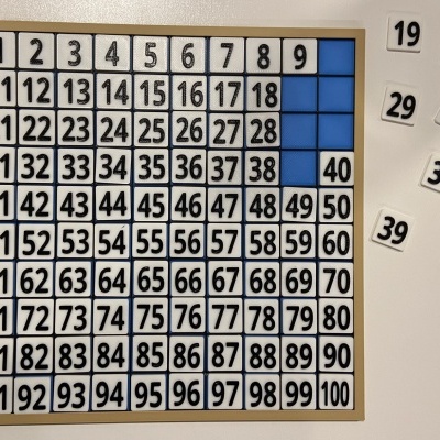 Quadro de números de 1 a 100 em cartolina com alguns números soltos em etiquetas arredondadas