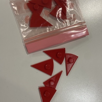 Peças triangulares vermelhas de plástico com botão circular, saco plástico transparente com fecho rosa