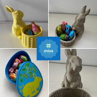 Coelhos decorativos com cestos de ovos de chocolate e caixa em forma de ovo azul com coelho amarelo e padrão floral.