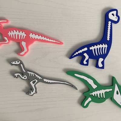 Figuras coloridas de dinossauros com esqueletos desenhados em branco sobre mesa de madeira.