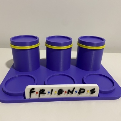 Conjunto de três recipientes roxos com tampas amarelas em base com placa FRIENDS