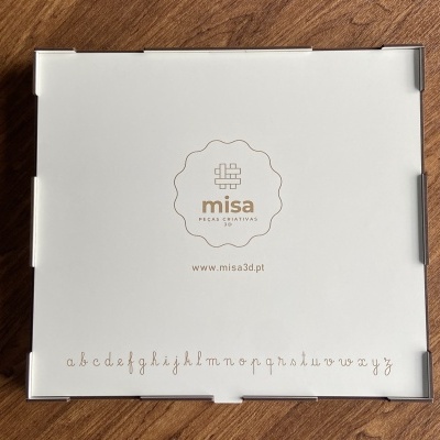 Caixa branca com logótipo misa e alfabeto manuscrito em fundo madeira