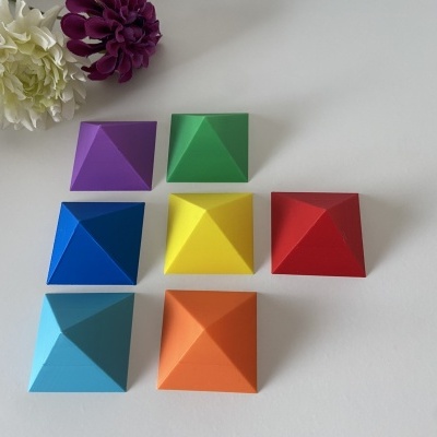 Set de pirâmides coloridas em superfície branca com flores ao fundo