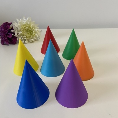 Sete cones coloridos em plástico dispostos em superfície branca com duas flores ao fundo
