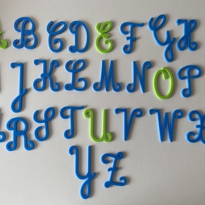 Letras do alfabeto em plástico azul e verde fixadas numa parede branca