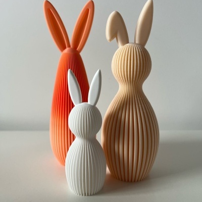 Três estatuetas decorativas de coelhos com textura canelada em laranja, bege e branco.