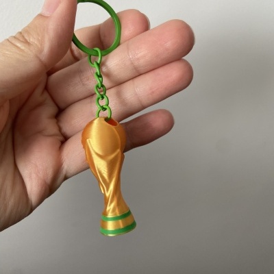 Porta-chaves com pendente em forma de taça dourada e verde nas mãos de uma pessoa.