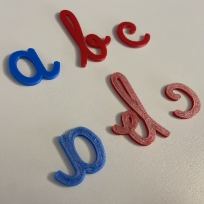 Peças de letras cursivas em plástico vermelho e azul sobre fundo branco