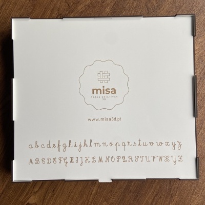 Caixa branca com logótipo 'misa' e alfabetos cursivos castanhos sobre madeira