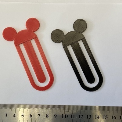 Marcadores de livros vermelhos e pretos em formato de cabeça com orelhas, sobre fundo branco e régua metálica.