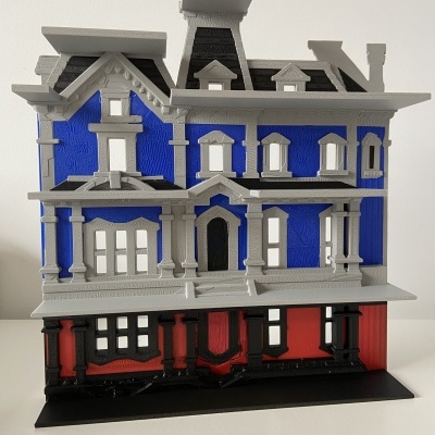 Casa de brincar azul, cinzenta e vermelha sobre base preta em fundo branco